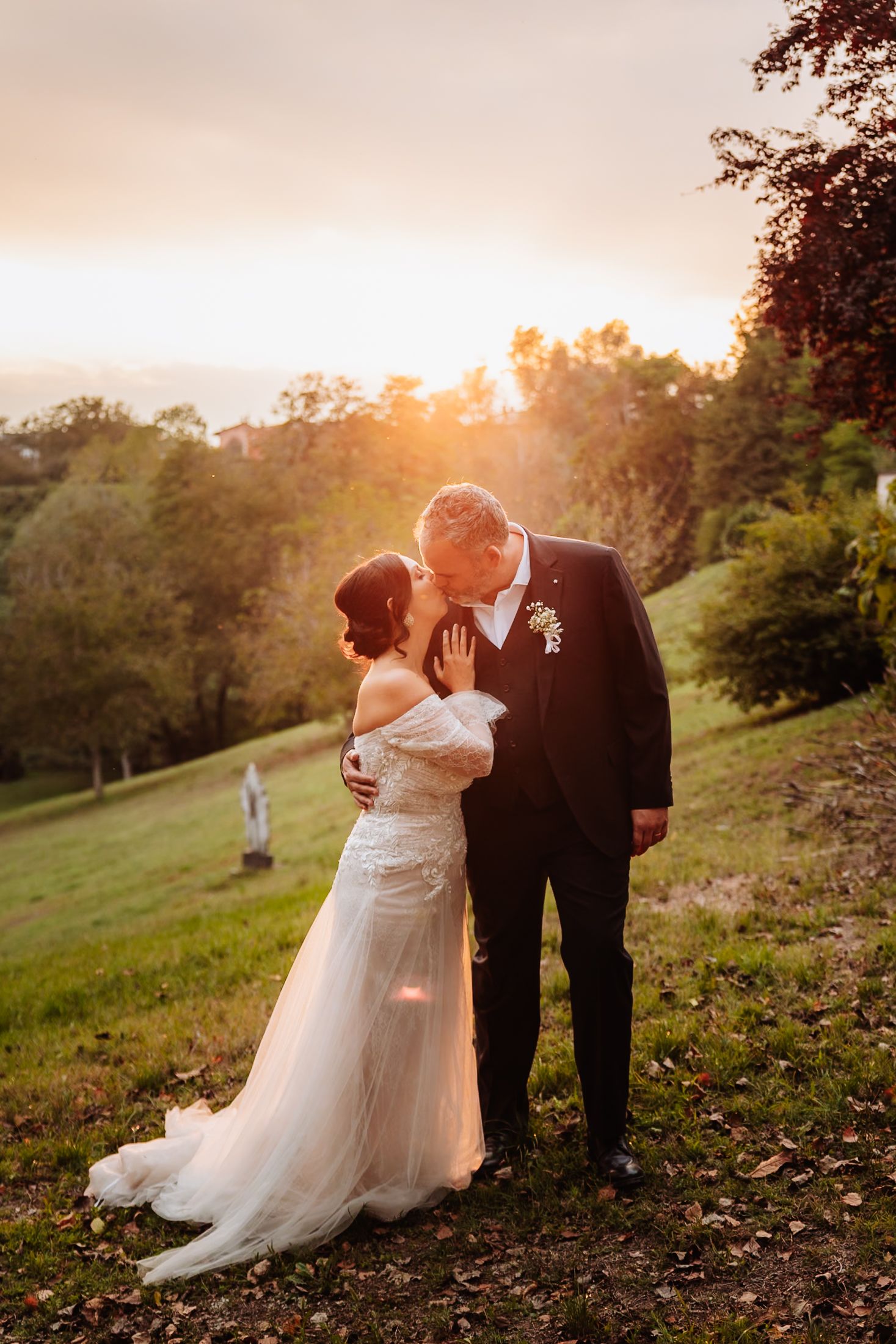 A couple in wedding attire shares an intimate moment at sunset on a hillside surrounded by autumn foliage.