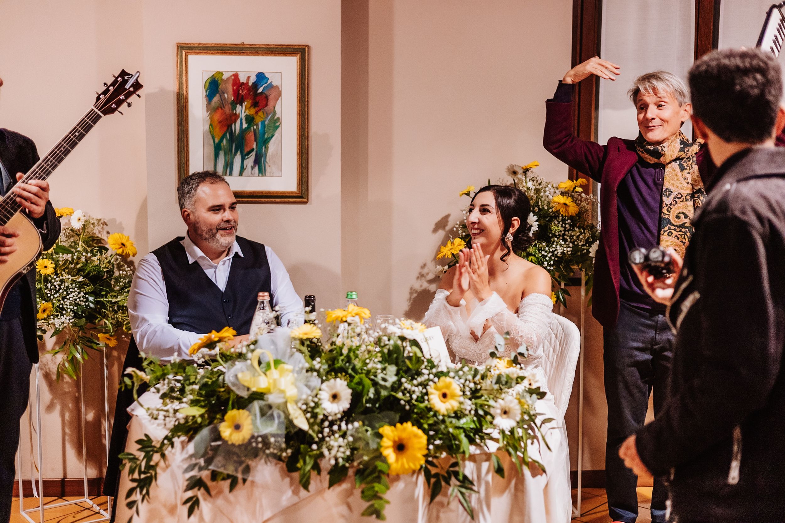 A wedding party celebrates during a reception with bright yellow sunflower and white floral decorations.