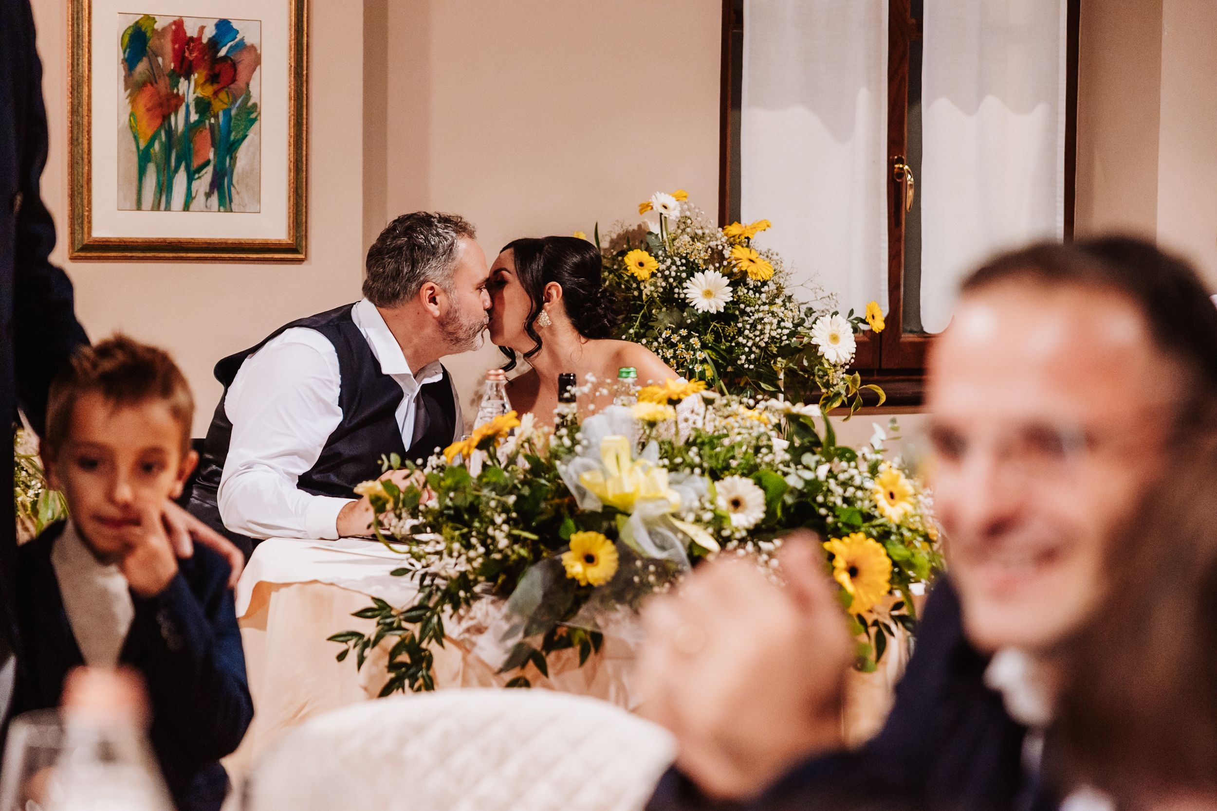 Wedding guests gathered at a reception table decorated with yellow and white floral centerpieces.