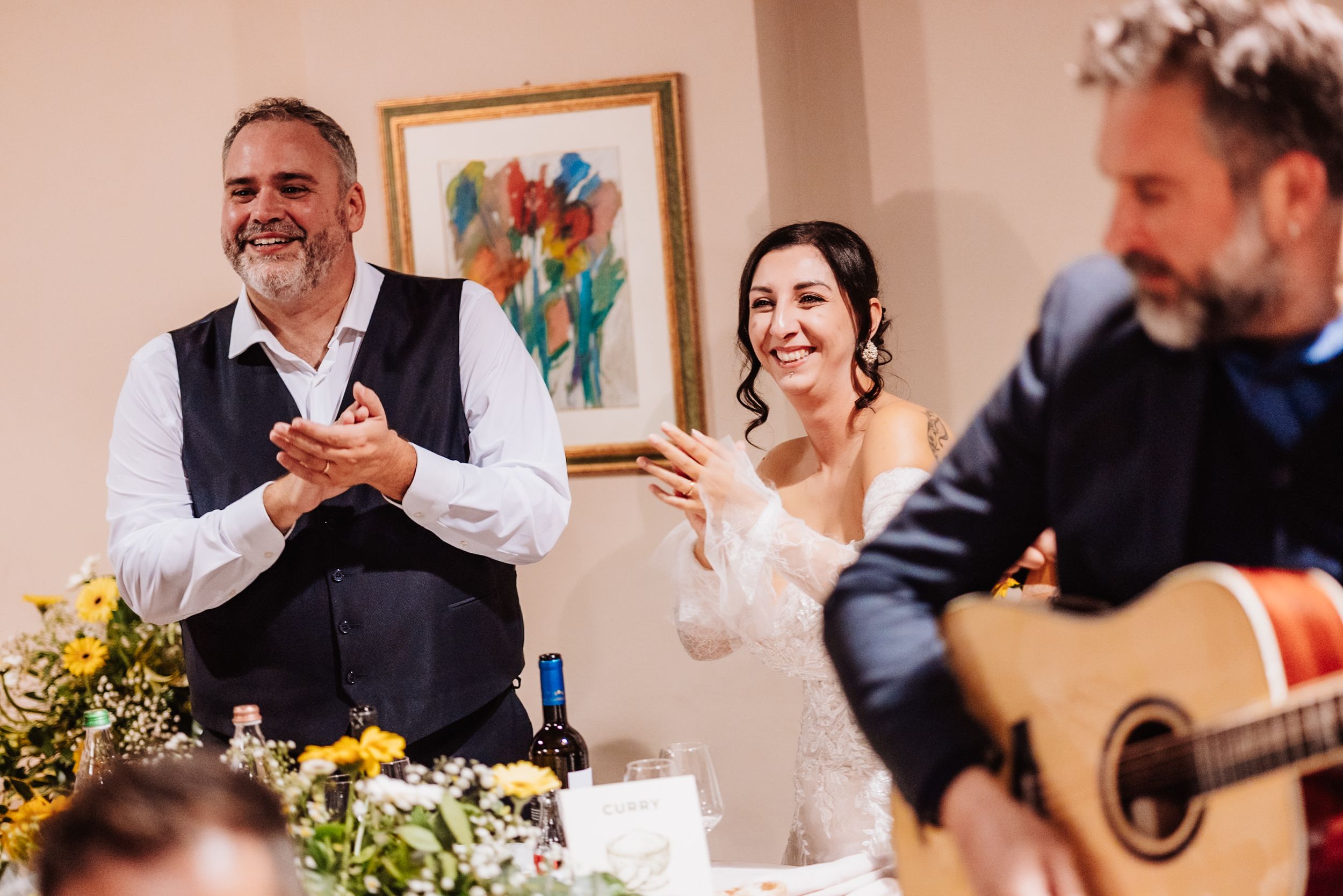 Wedding guests laugh and share joyful moments during a reception celebration at an indoor venue.