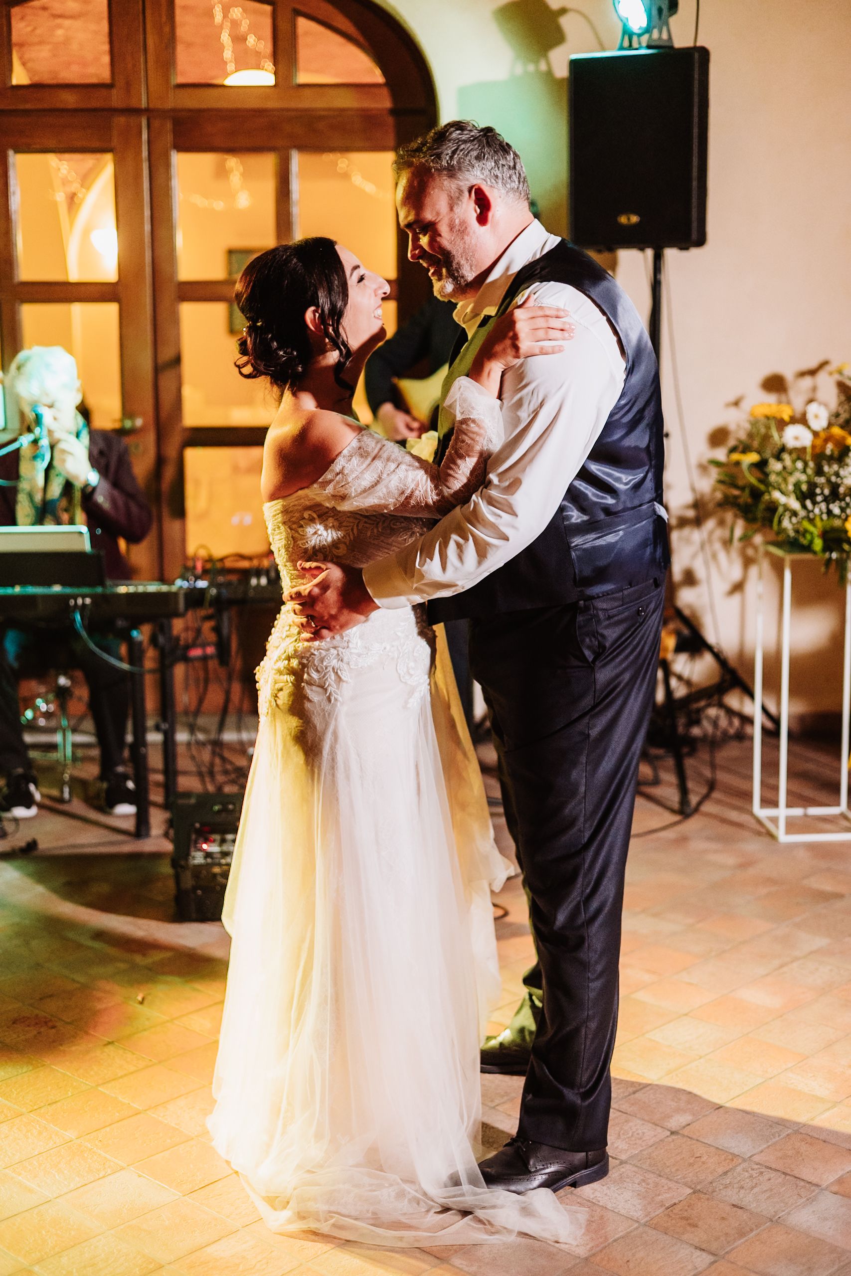 A couple shares a romantic first dance at their wedding reception in a warmly lit venue with tiled floors.