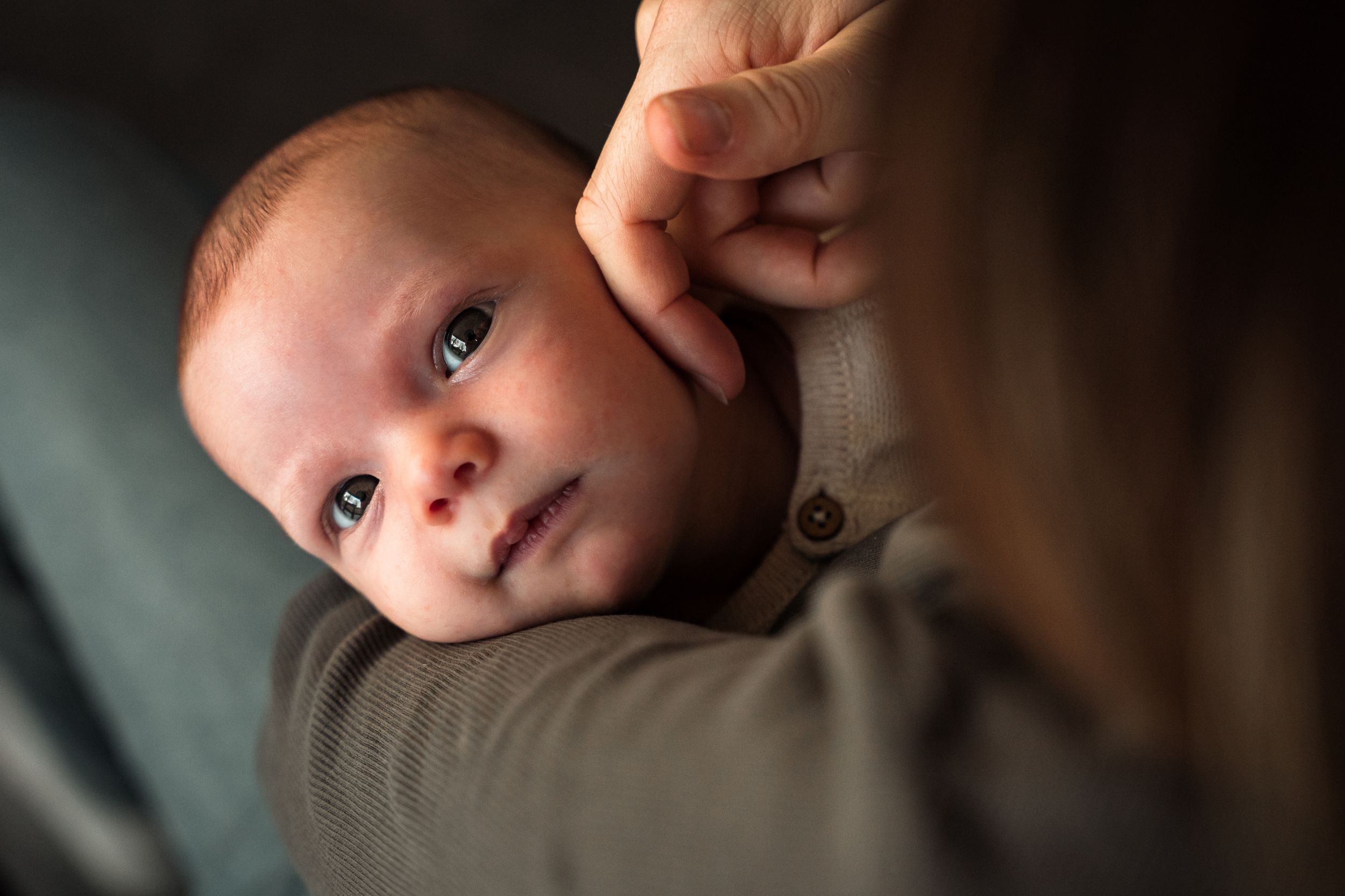A baby with bright eyes gazes at the camera while being held in olive green clothing.