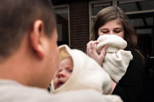 People share a light moment together while wrapped in cozy white blankets outside a brick building.