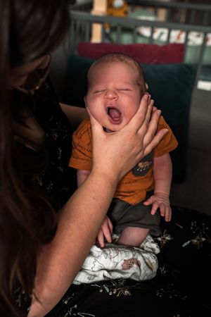 A sequence of photos showing hands holding a laughing baby wearing a white onesie against a dark background.
