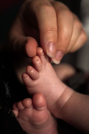 Close-up series showing tiny baby toes and feet being gently touched and held against a dark background.