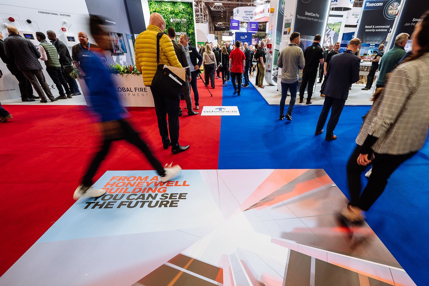 Trade show floor with exhibition booths and attendees walking between displays.