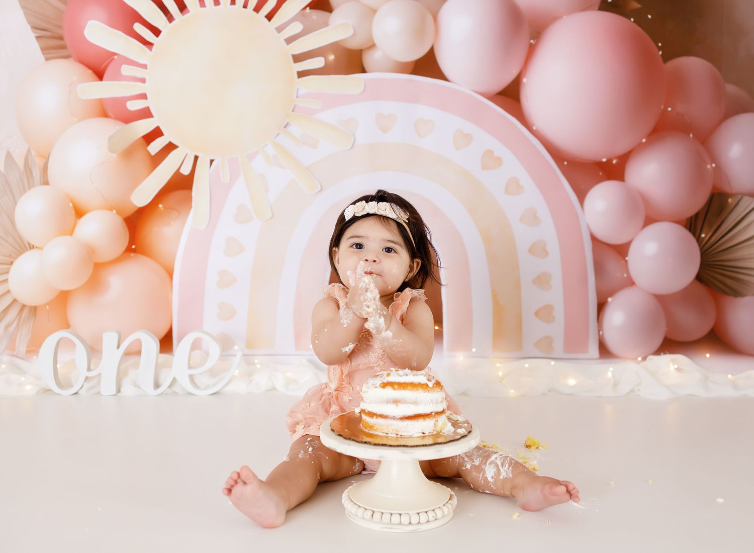 Pink and white balloon arch with cake display setup for a special celebration against a light colored wall.