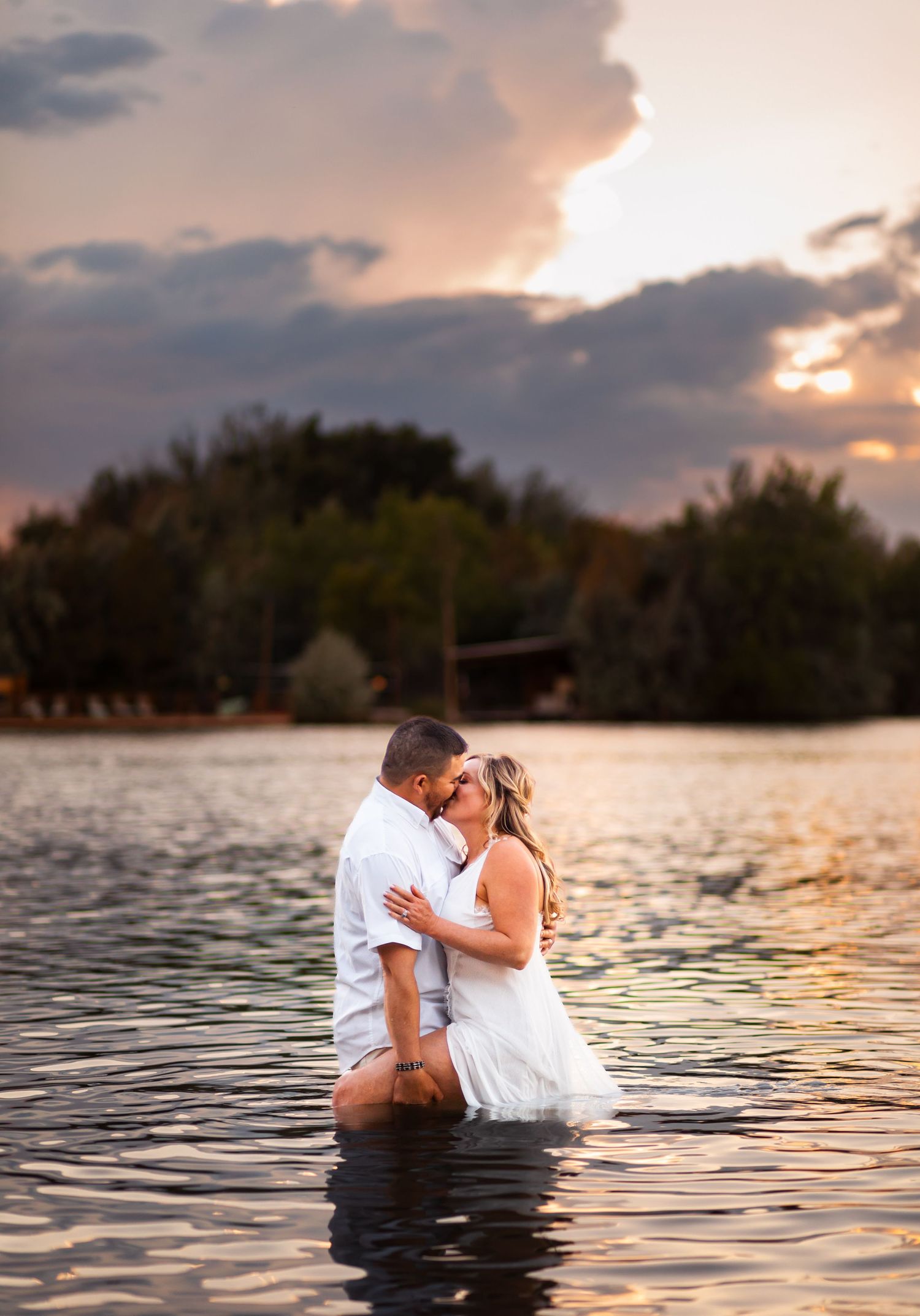 Bride and Groom holding each other close standing in a lake for sunset portraits in Fort Collins, Colorado.