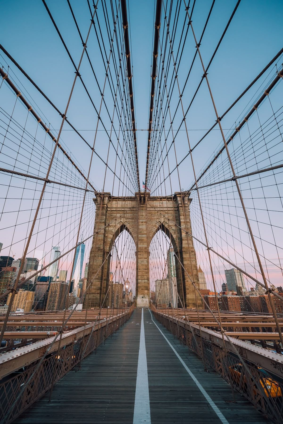 Iconic Brooklyn Bridge walkway with steel cables and stone arches against blue sky in New York City.