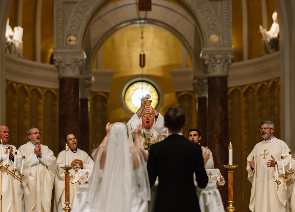 A traditional Catholic wedding ceremony takes place inside an ornate cathedral with golden arches and religious figures present.