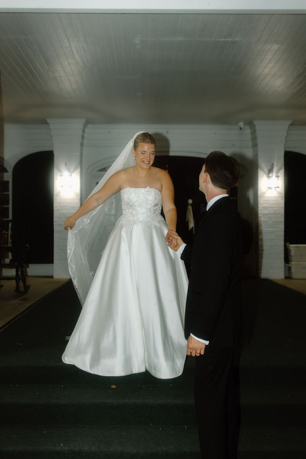 A couple in wedding attire dances together in a dimly lit outdoor venue at night.