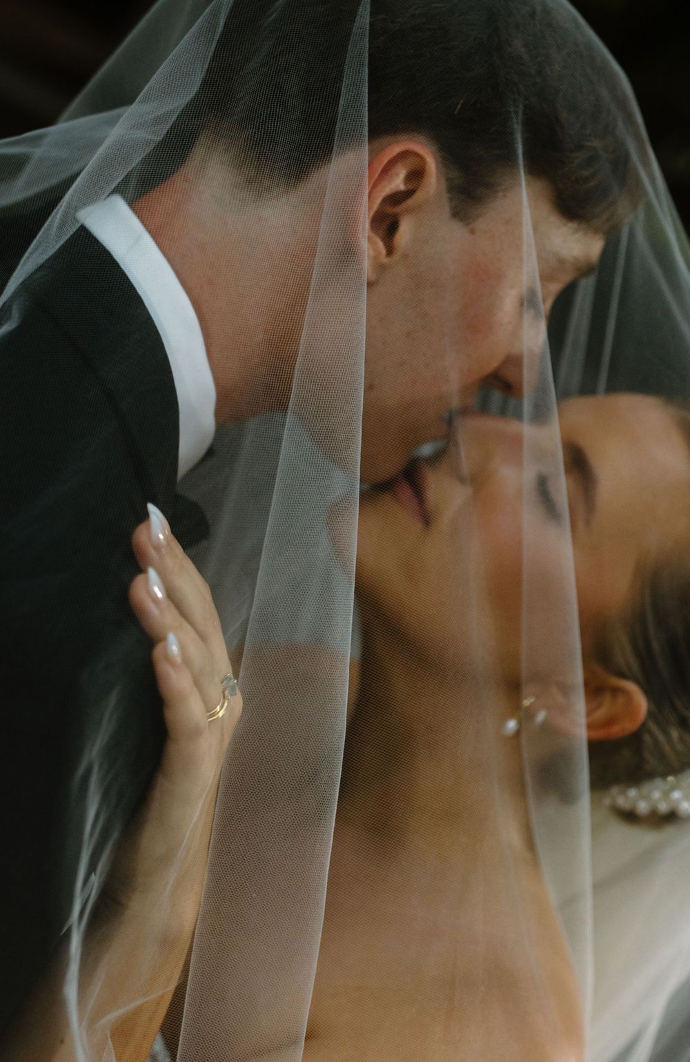 A romantic wedding moment captured through delicate white veil as couple shares an intimate kiss.