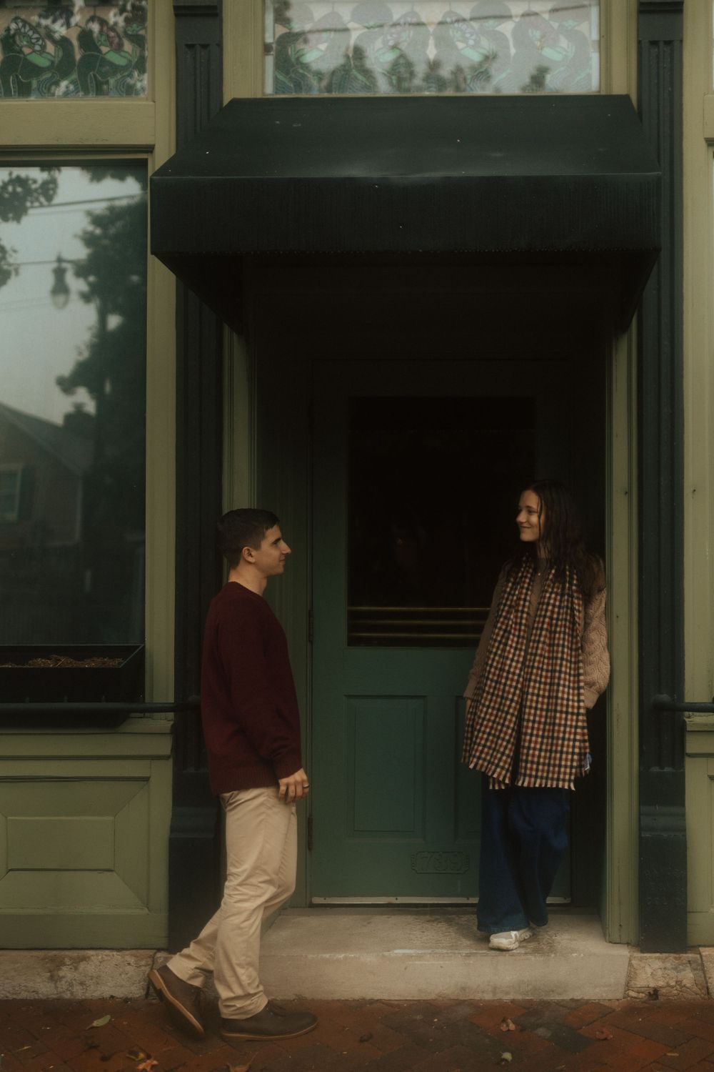 Two people stand in a doorway of a building with green doors and beige walls in a series of sequential photos.