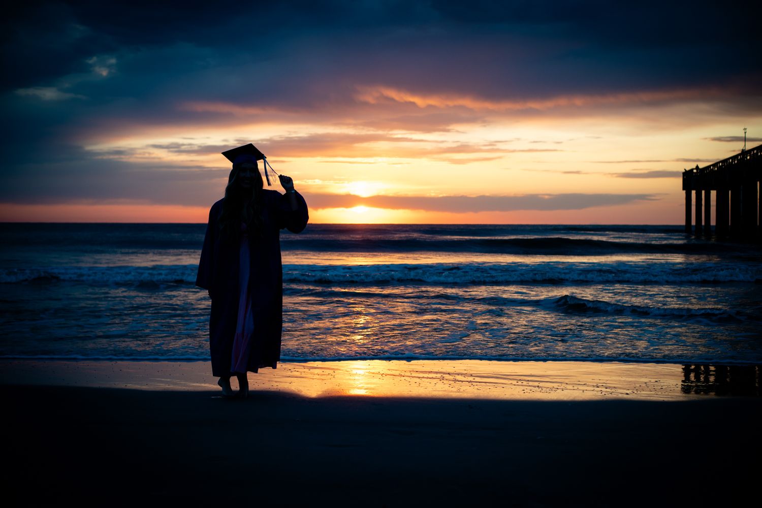 A silhouetted figure stands on a beach at sunset with dramatic orange and purple clouds reflecting on the ocean water.