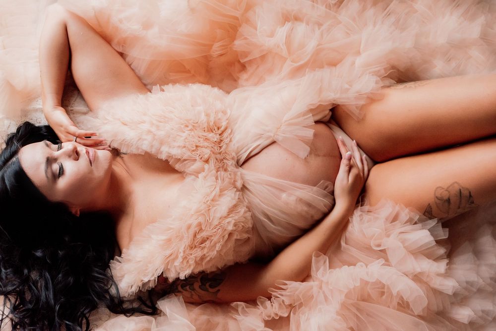 Woman in a peach tulle gown lying gracefully surrounded by soft ruffled fabric.
