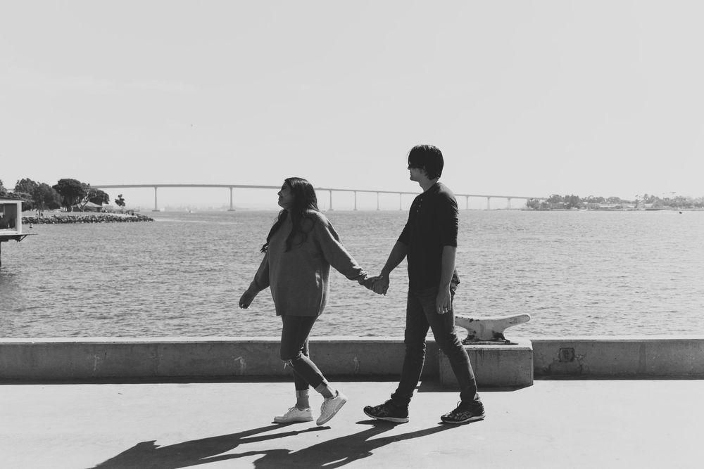 A black and white photo of a couple walking on the pier in San Diego during their engagement photo shoot