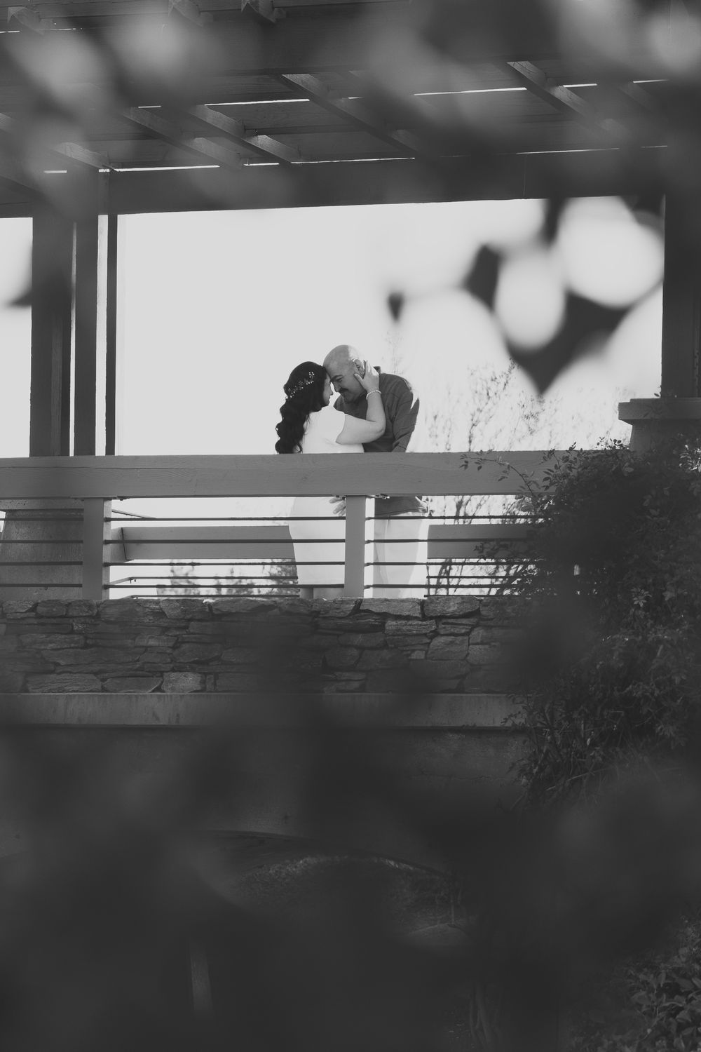 Black and white photo of engaged couple about to kiss while on a bridge
