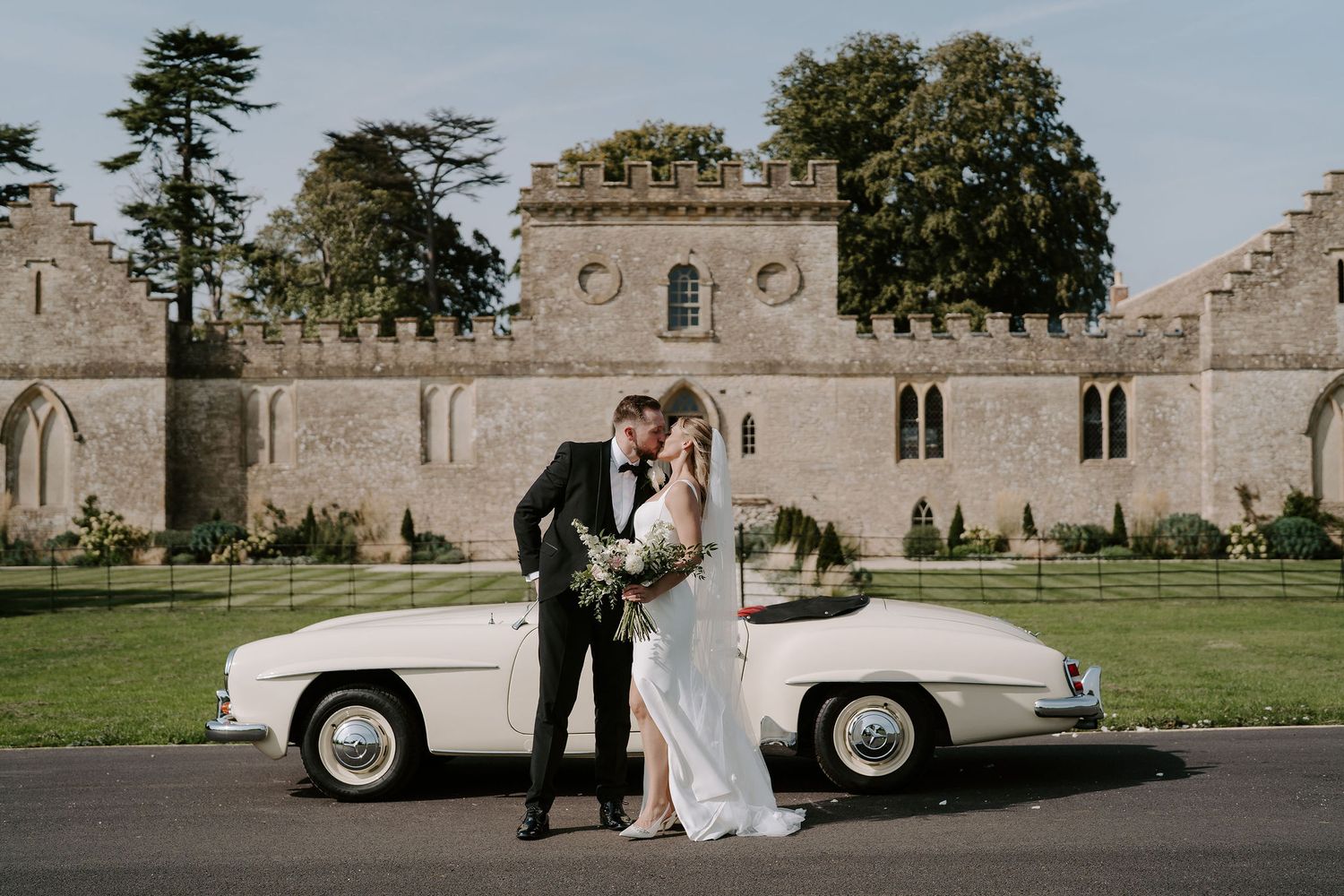 bride and groom kissing by wedding car at ivy lodge in cirencester