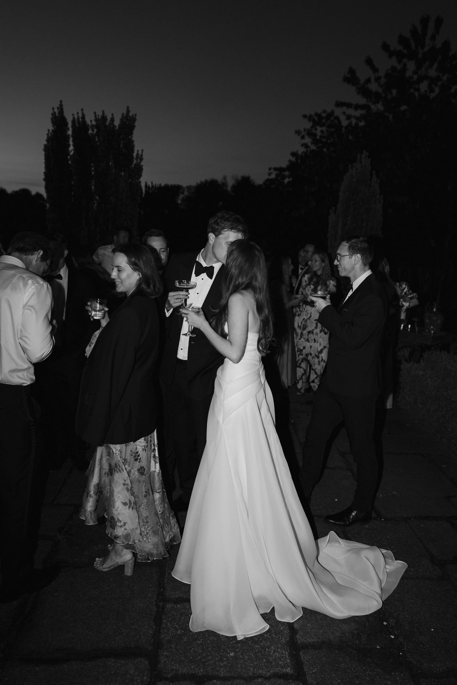 bride and groom sharing a kiss during their cocktail hour while their guests surround them drinking cocktails at dewsall court in hereford
