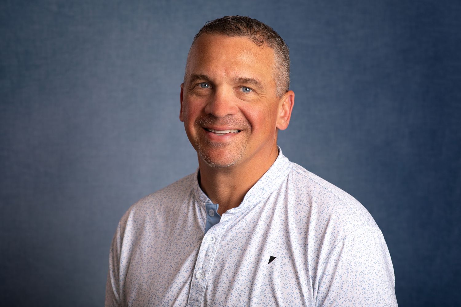 A professional headshot showing someone in a white dress shirt against a dark blue background.