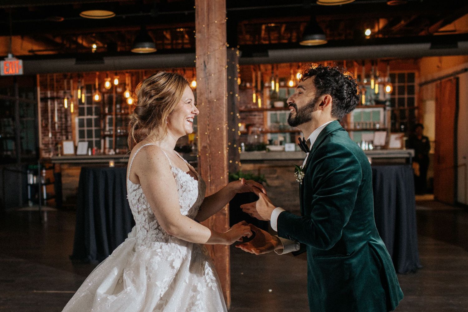 A couple shares their first dance in a rustic industrial venue with exposed brick walls.
