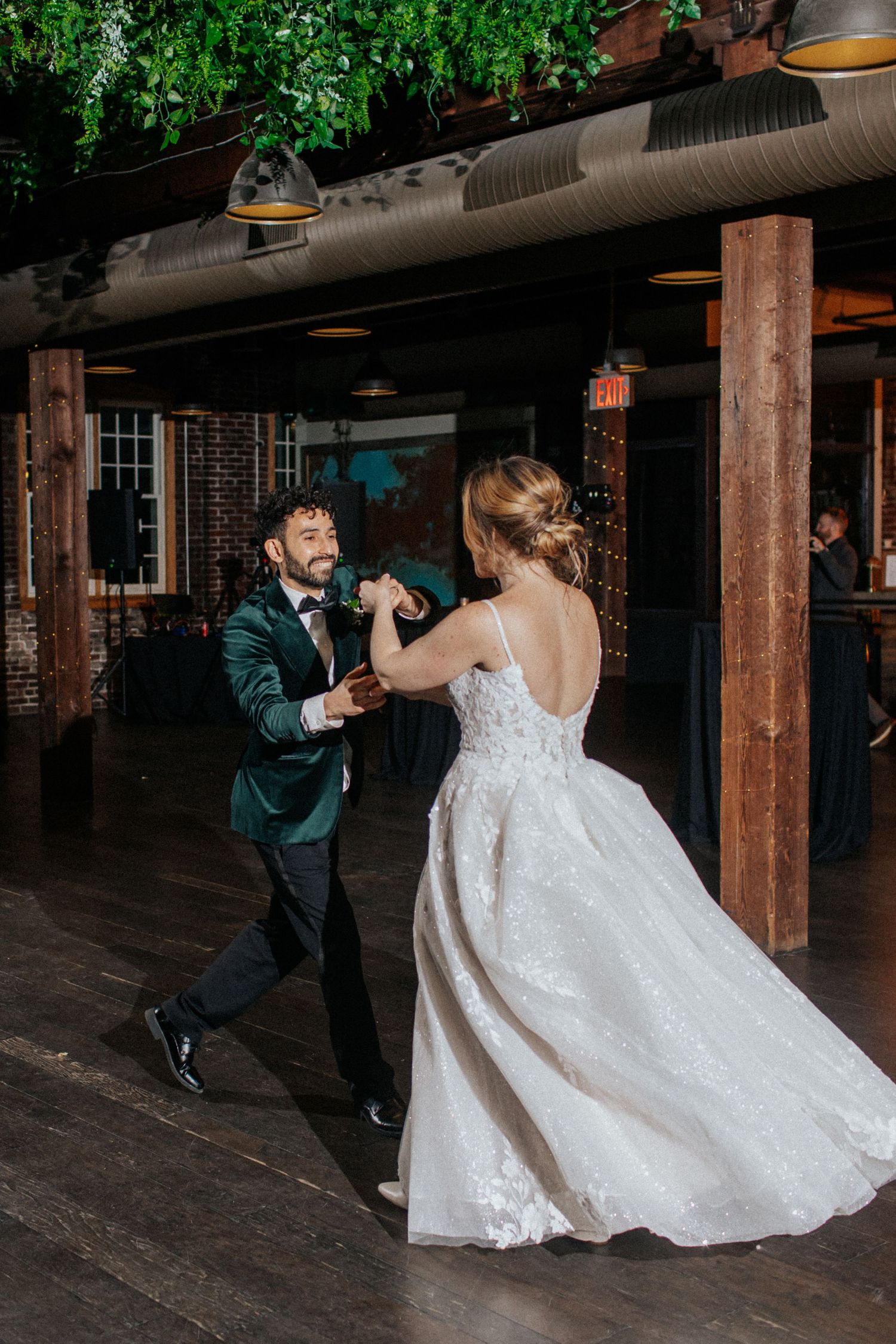 Bride in white gown twirls during a playful dance moment at an industrial-style venue.
