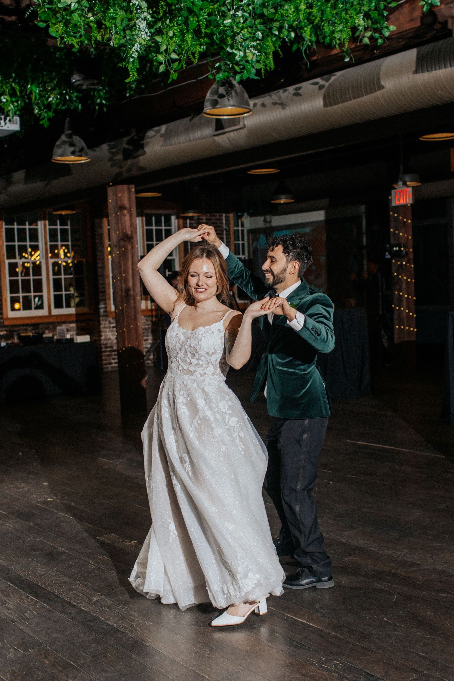 Newlyweds dancing together on a wooden floor with greenery hanging from the ceiling.