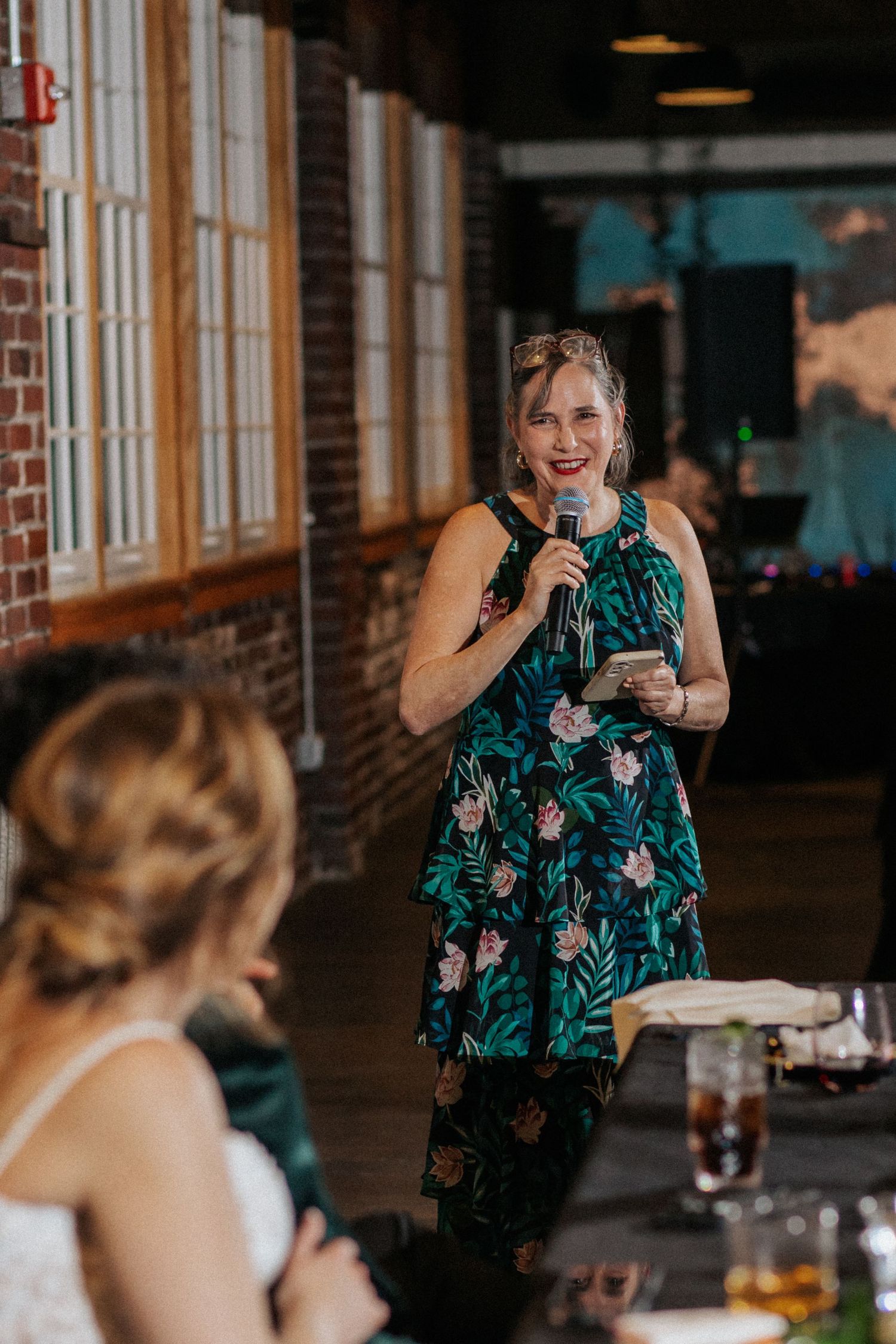 Wedding guest in floral dress gives an animated toast during the reception.