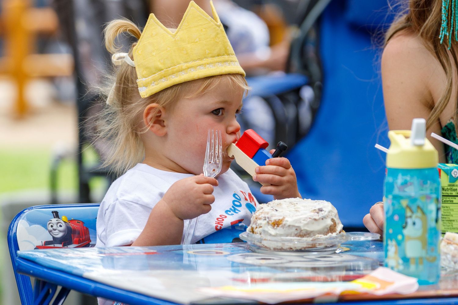 Children eating cake and snacks at an outdoor birthday party with blue decorations and party supplies.
