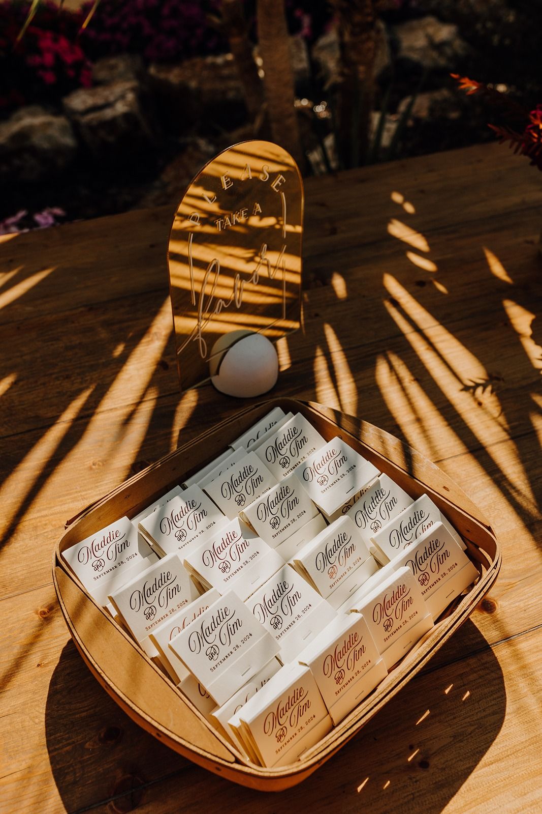Custom wedding matchbooks arranged on wooden table with diagonal shadows cast across the surface at River Garden Weddings and Events.