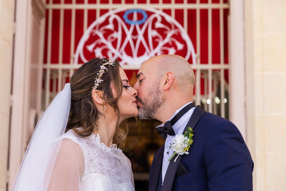 Bride and groom sharing a romantic kiss in front of a decorative red church gate on their wedding day.