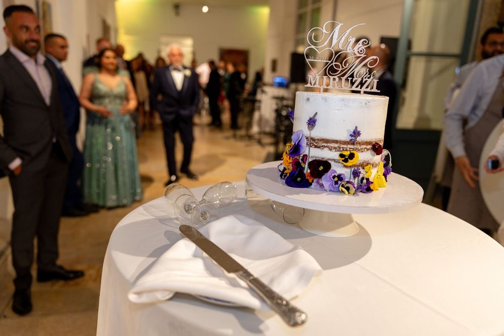 Elegant two-tier wedding cake with floral decorations and Mr & Mrs topper on white table at reception.
