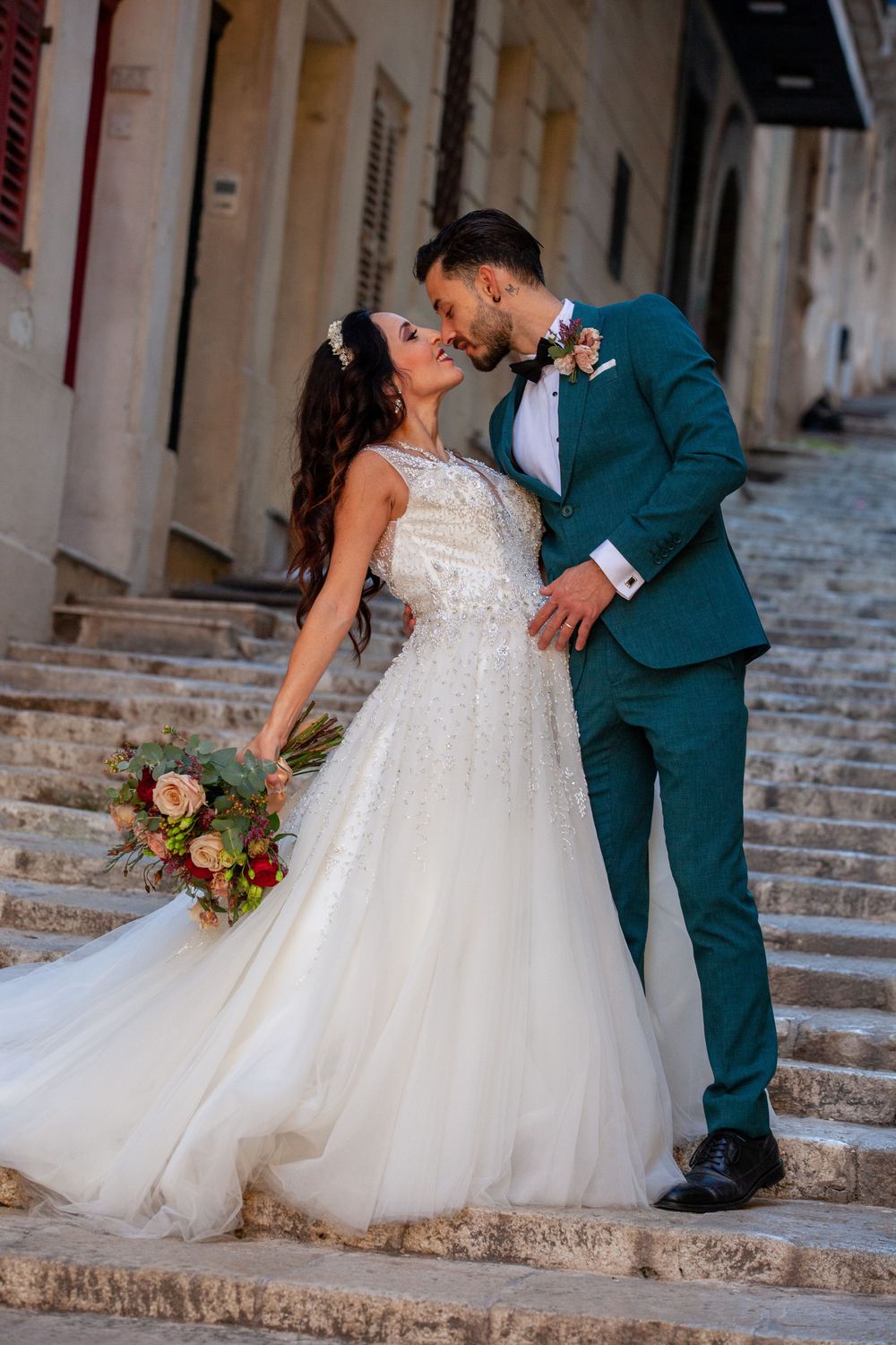 Bride and groom sharing a romantic kiss on stone steps in an elegant European street.