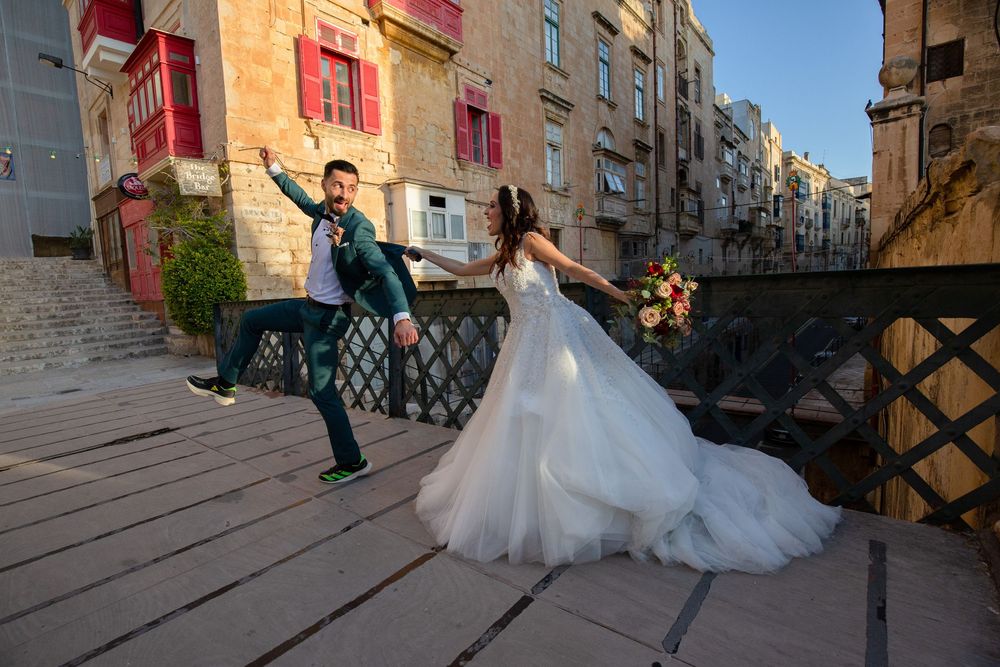 Joyful bride and groom dancing on a bridge in a historic European city, with colorful balconies in the background.