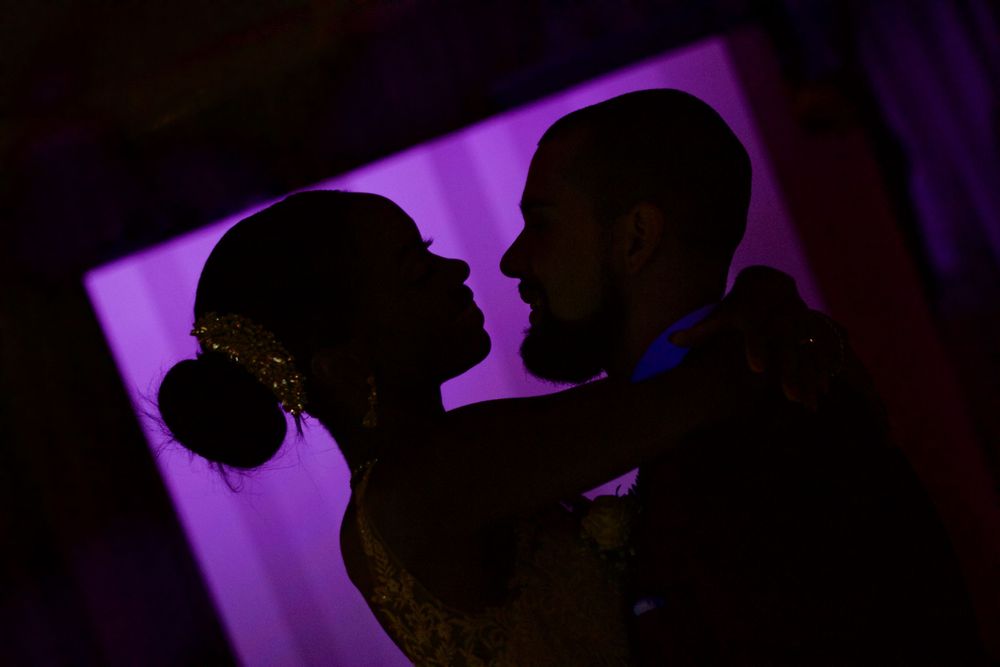 Silhouette of a bride and groom sharing a romantic first dance bathed in purple light at their wedding reception.