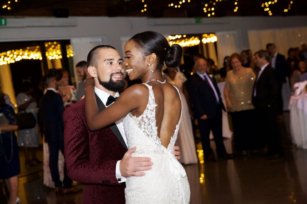 Bride and groom share first dance in elegant wedding venue with warm string lights.