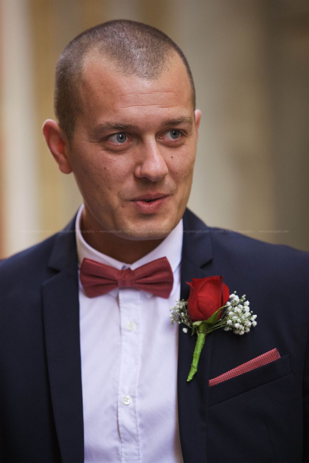 Formal portrait showing groom wearing black suit with red bowtie and boutonniere.