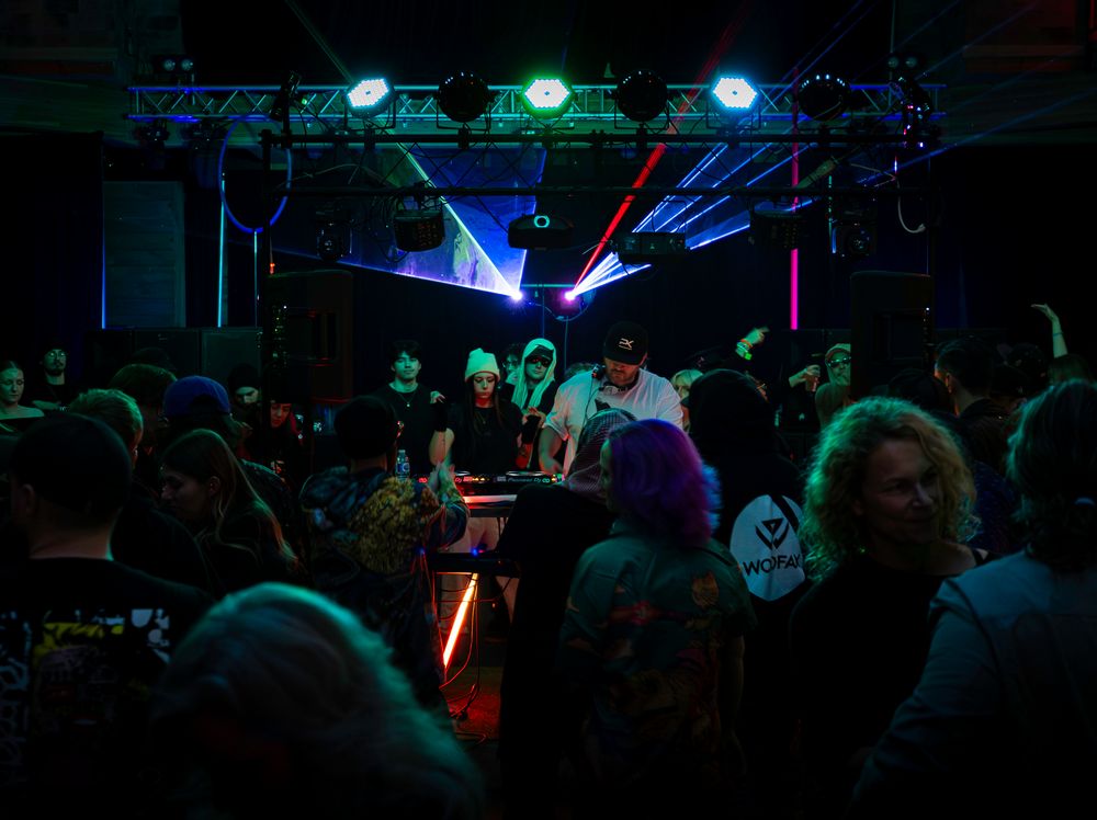 Colorful lights illuminate a dark nightclub dance floor filled with people enjoying music and dancing.