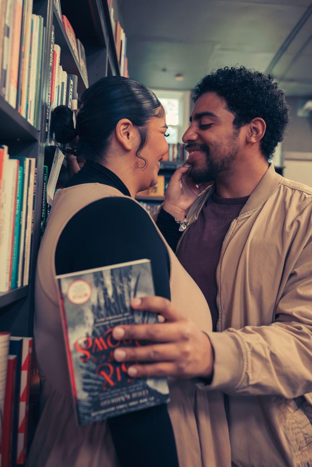 A romantic couple shares an intimate moment while holding a book in a library setting.