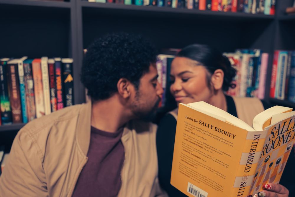 A romantic moment between two people in a dimly lit library surrounded by books.