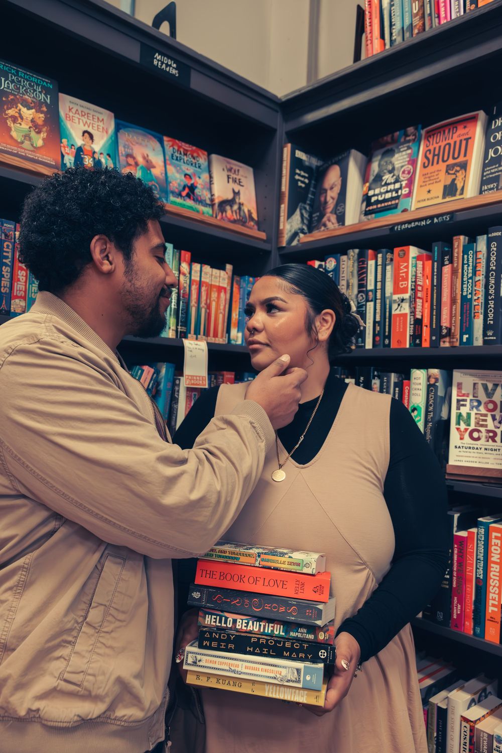 Two people share an intimate moment while browsing books in a cozy bookstore corner.