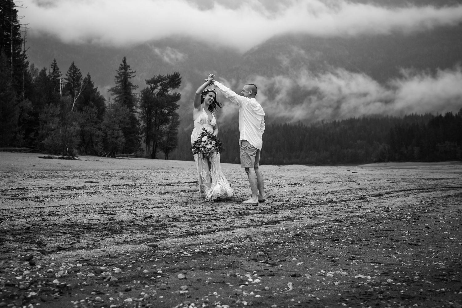 A couple dancing together on a mountain meadow with dramatic clouds and forest in black and white.