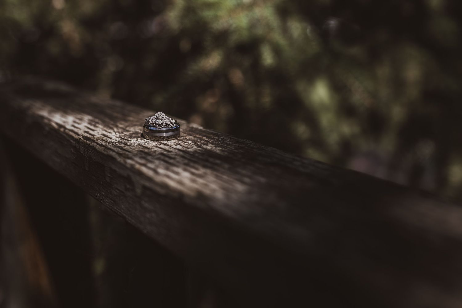 A small engagement ring sits on a dark wooden surface with soft bokeh background lighting.