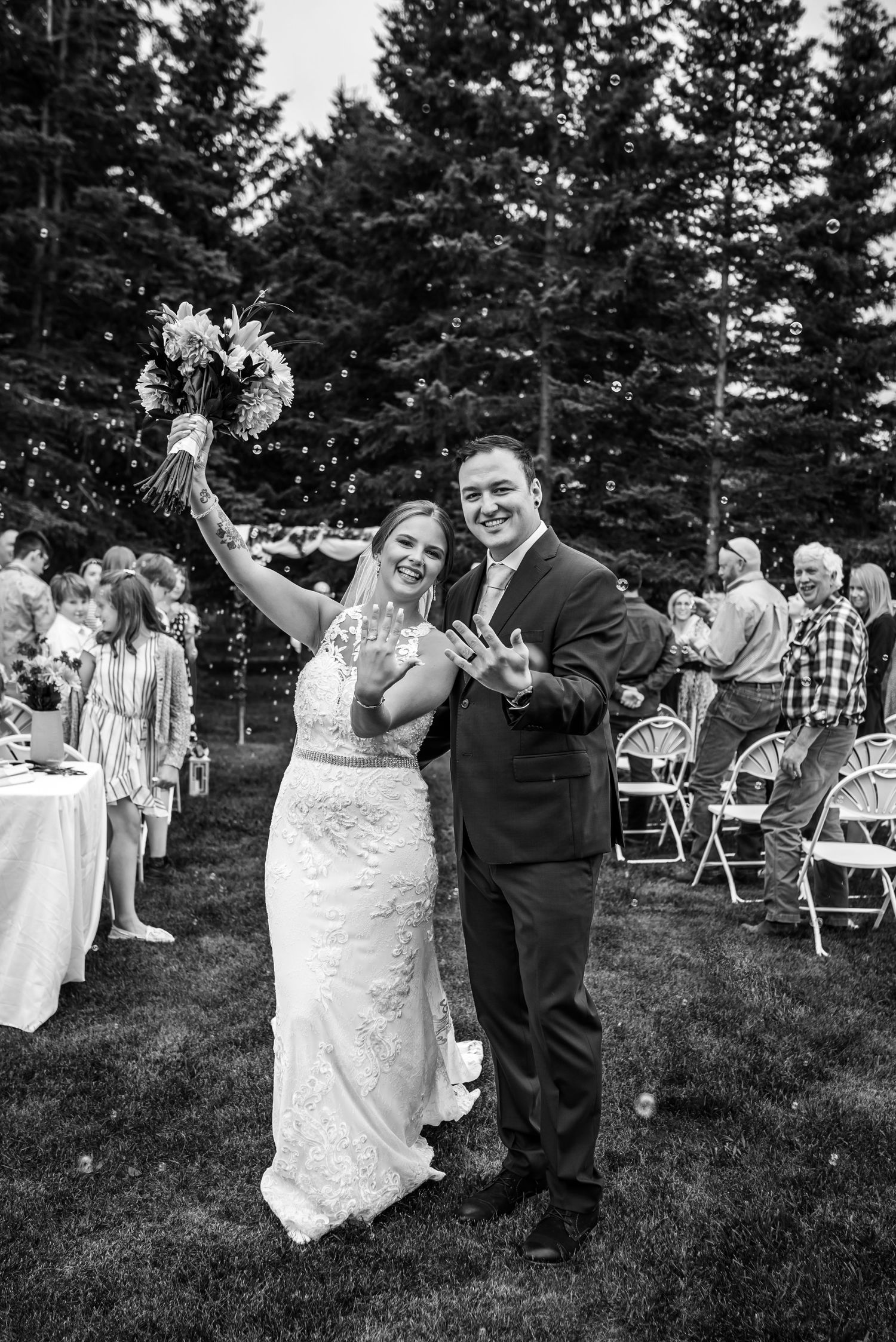 A couple shares a joyful dance moment at an outdoor wedding reception with pine trees in the background.