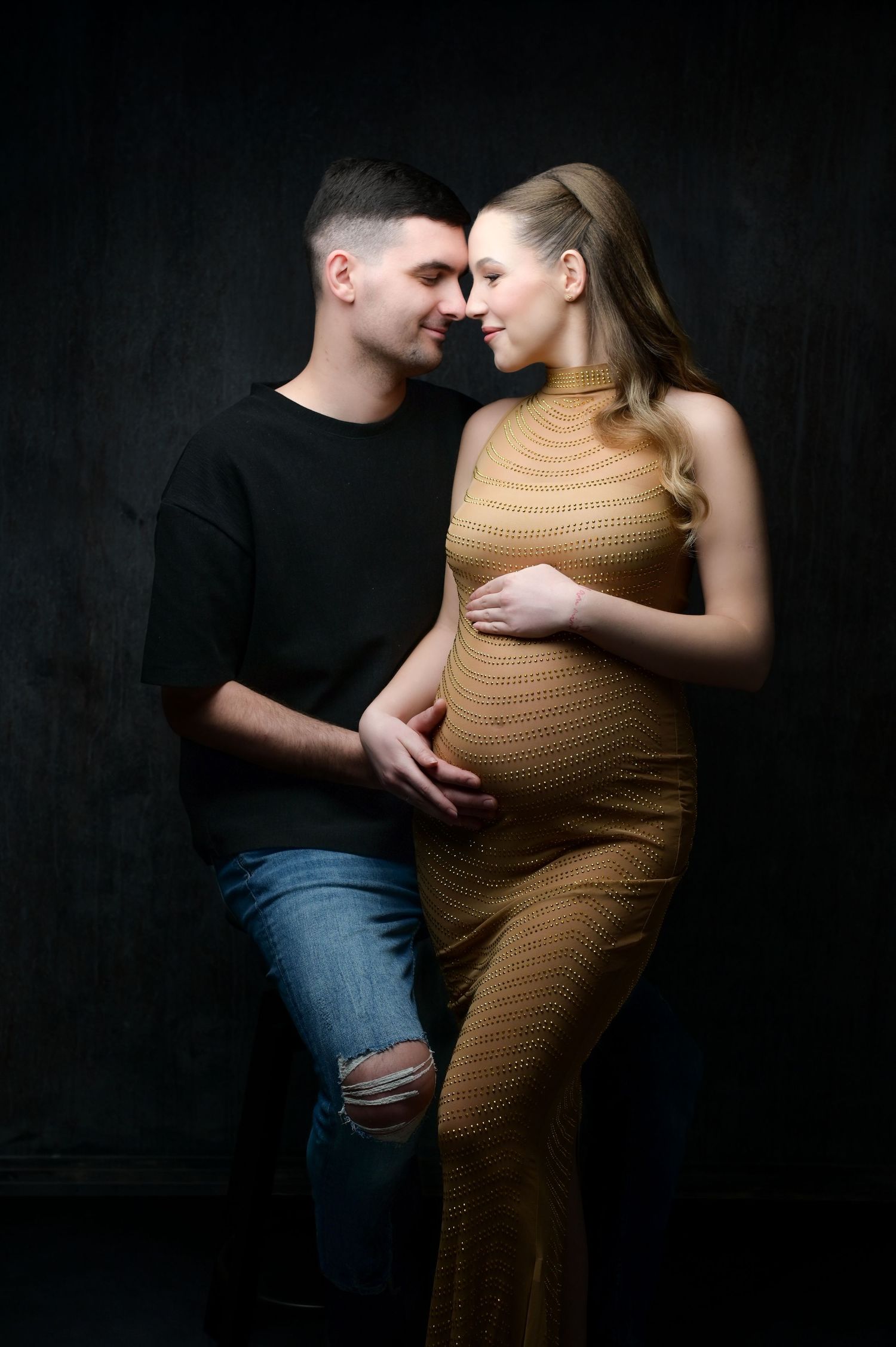 Intimate maternity photo series showing couple embracing against dark background in romantic poses.