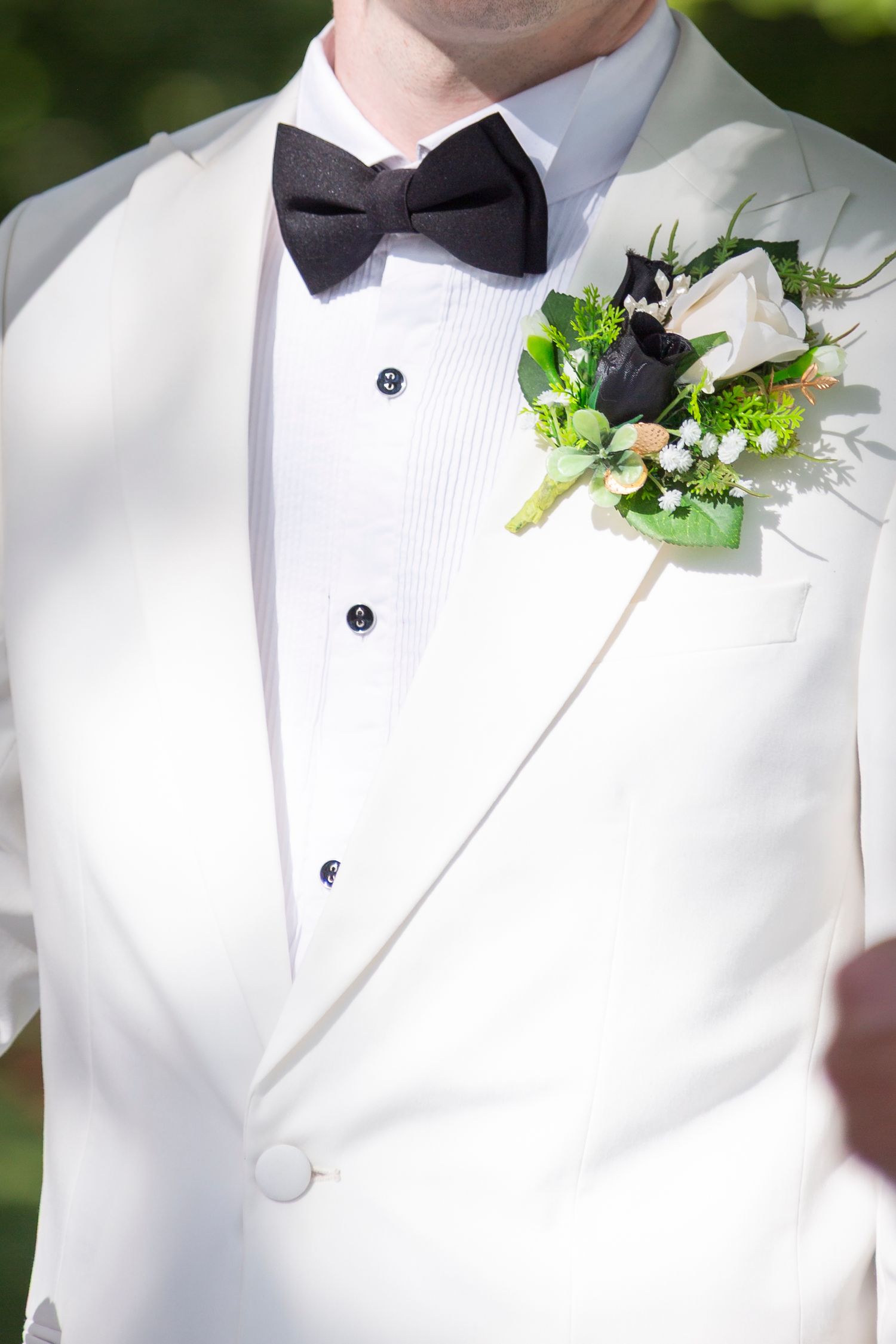 Close-up details of white tuxedo jackets with black bow ties and green floral boutonnieres at a formal event.