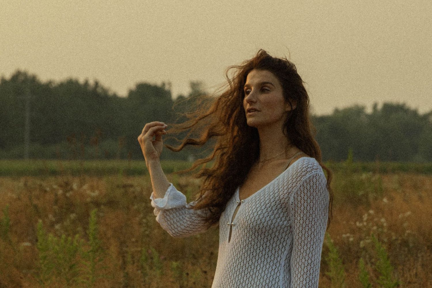 Young woman in white dress standing in golden field with wind blowing her hair.