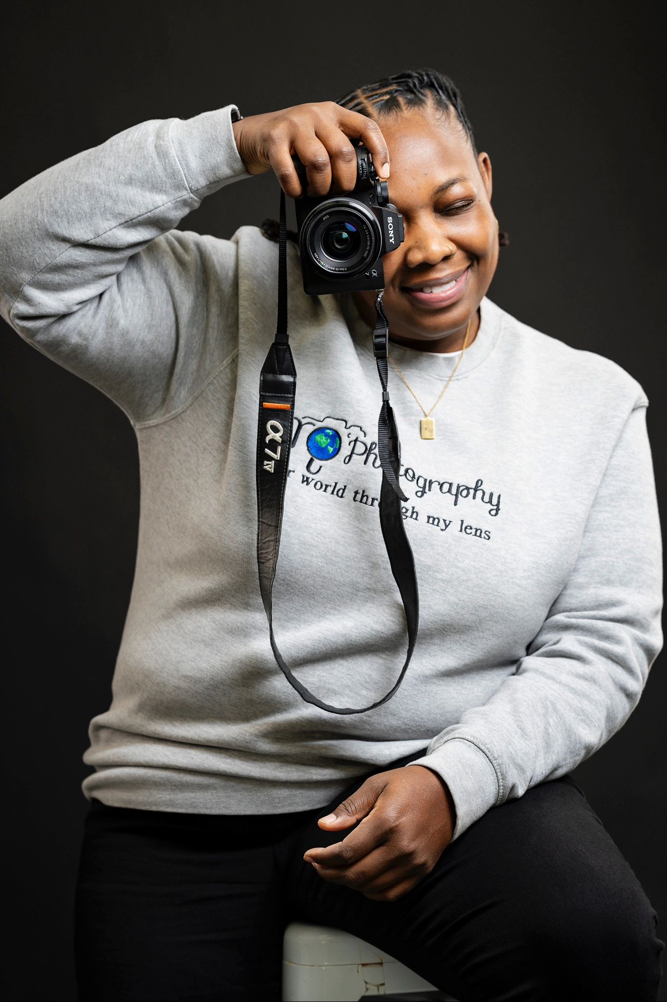 Person in grey sweatshirt holding camera against dark background in creative portrait series.