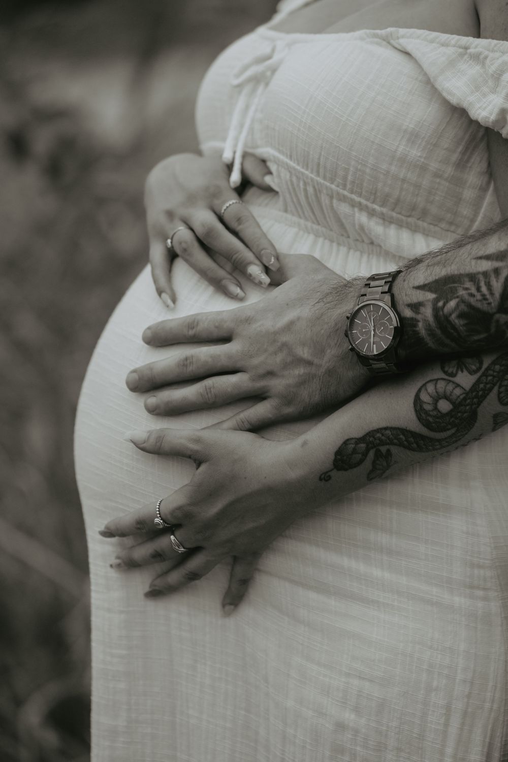 Close-up shots of hands tenderly cradling a pregnant belly, showing tattoo details in black and white.