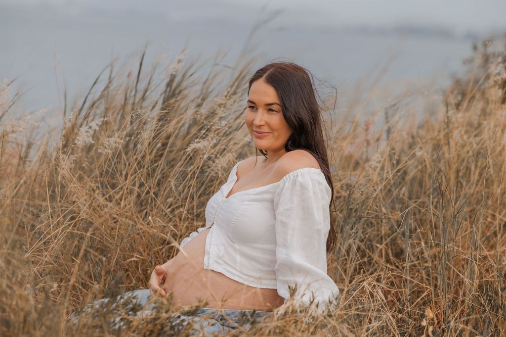 A person in a white dress sits among tall golden grass in a dreamy outdoor setting during golden hour.